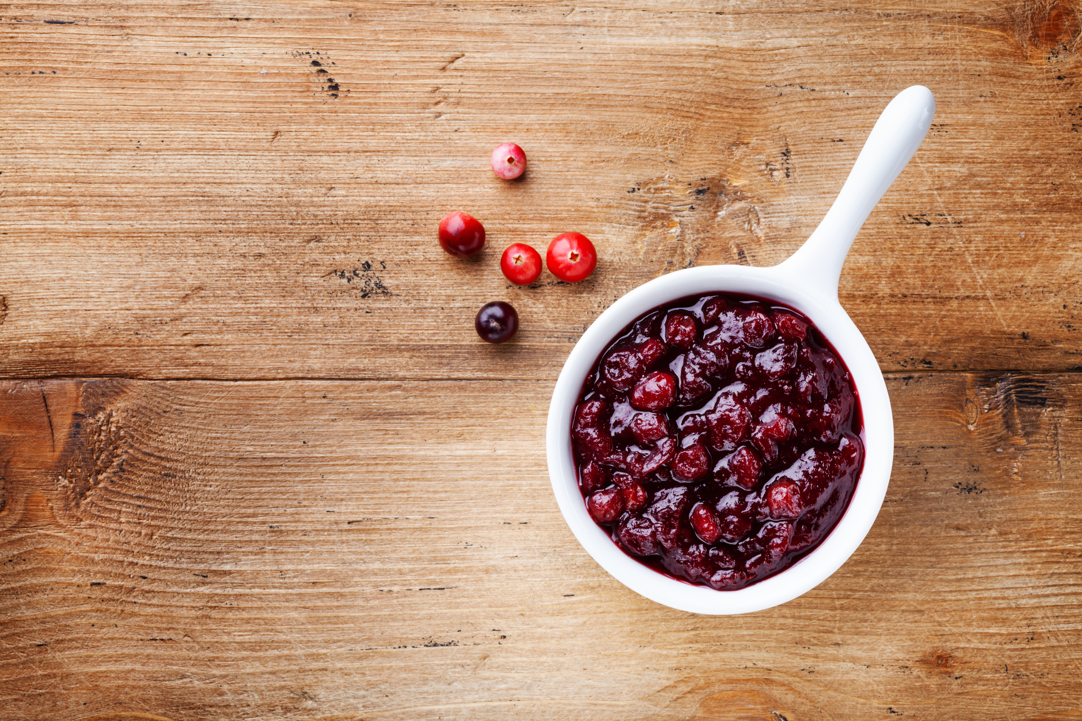 Cranberry sauce in ceramic saucepan with berries on wooden table top view.