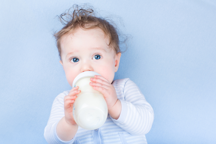 Sweet baby with blue eyes drinking milk in plastic bottle