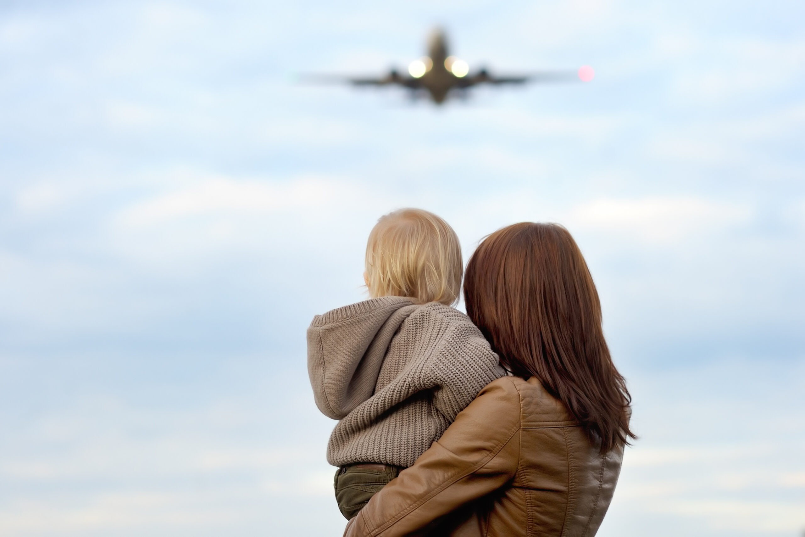 Woman holding toddler with airplane on background