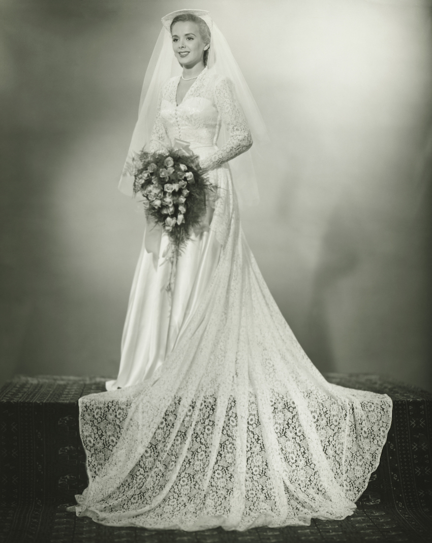 Young woman wearing wedding dress standing in studio, (B&W)