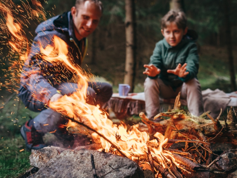 Father and son warms near campfire in forest