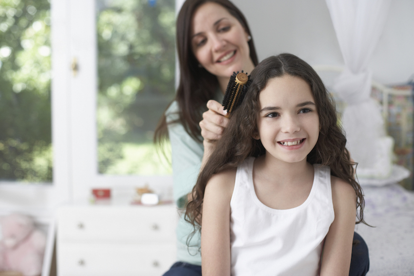 Young girl in bedroom having hair brushed by woman and smiling