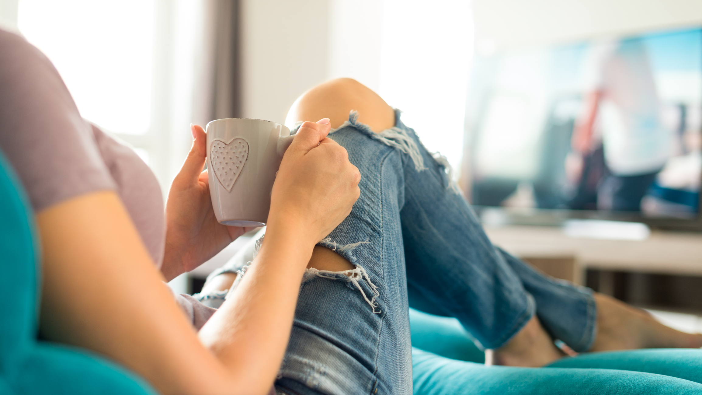 Young woman relaxing on the sofa, watching tv drinking coffee