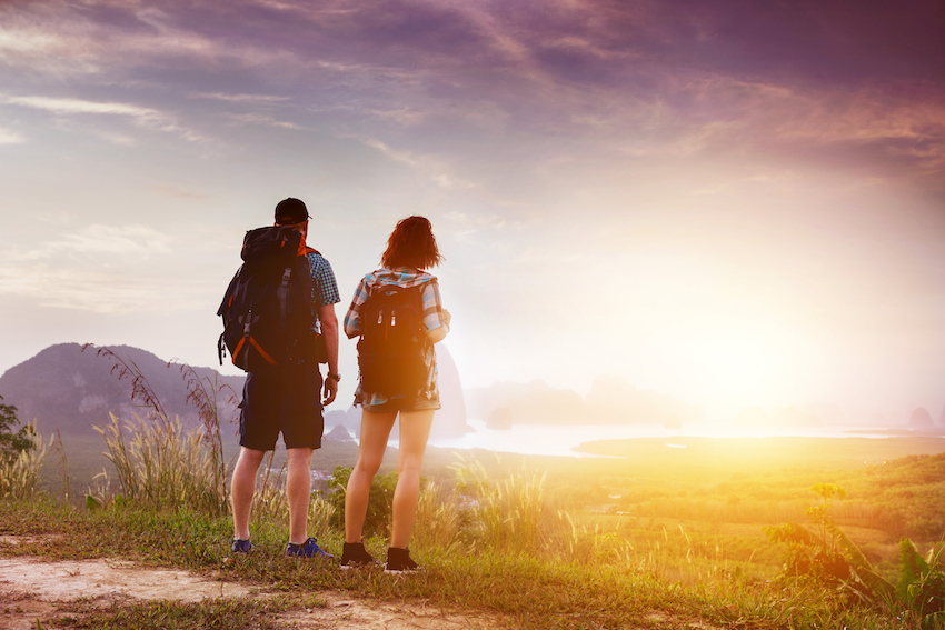 Couple backpackers watch at sunrise or sunset near sea bay and islands