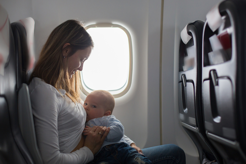 Young mom, playing and breastfeeding her toddler boy on board of aircraft