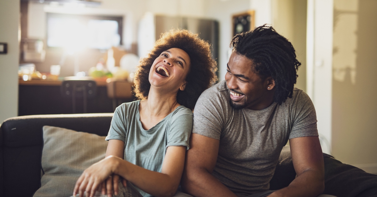 Cheerful black couple having fun while relaxing on sofa at home.