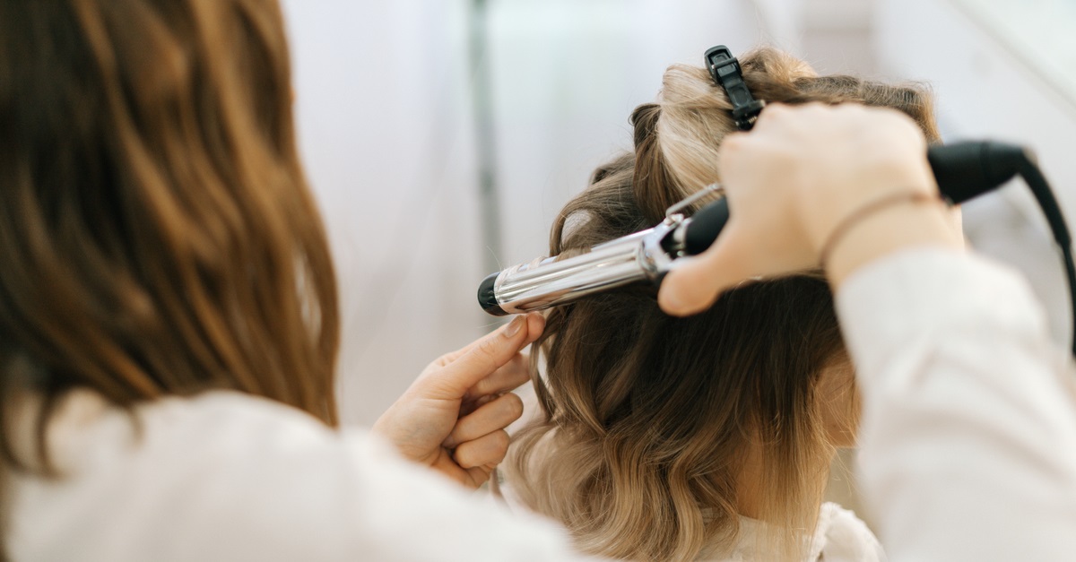 Female hairdresser making hairstyle for young woman with blonde hair in salon.