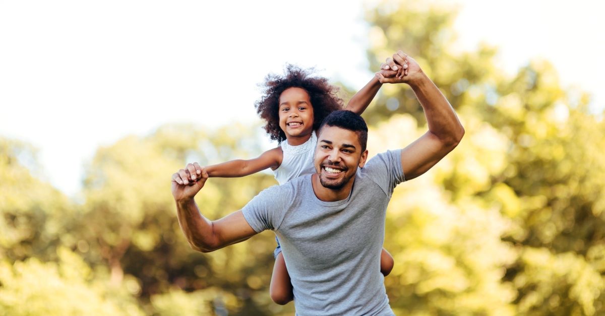 Portrait of young father carrying his daughter on his back in nature