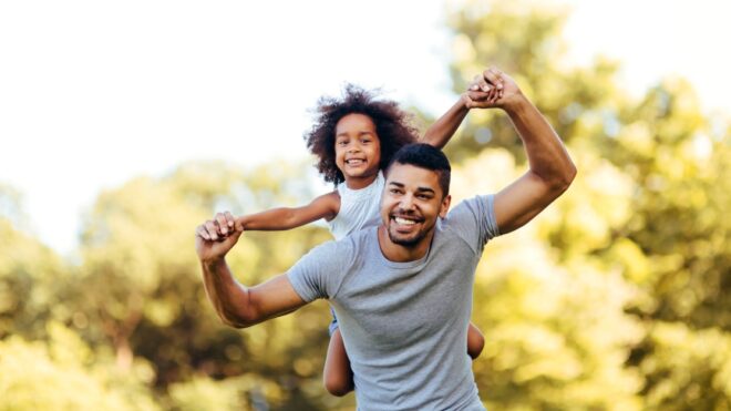 Portrait of young father carrying his daughter on his back in nature