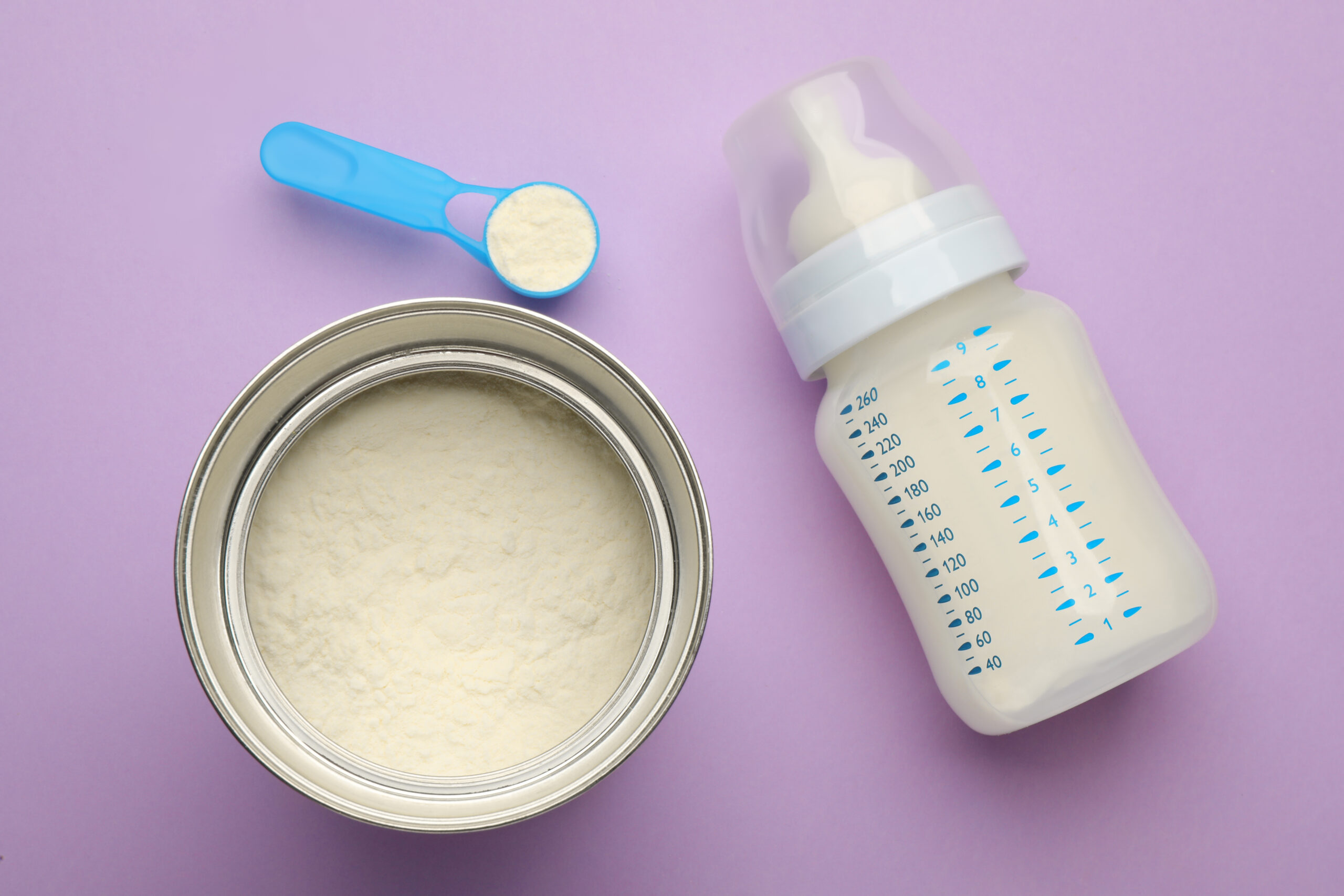 Feeding bottle with infant formula and powder on violet  background, flat lay