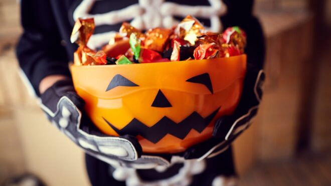 Boy in skeleton costume holding bowl full of candies