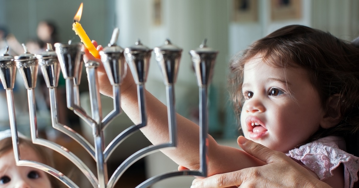 Young girl lights the Hanukkah menorah with help from adult