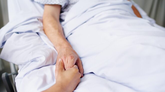 Holding person's hand in hospital bed