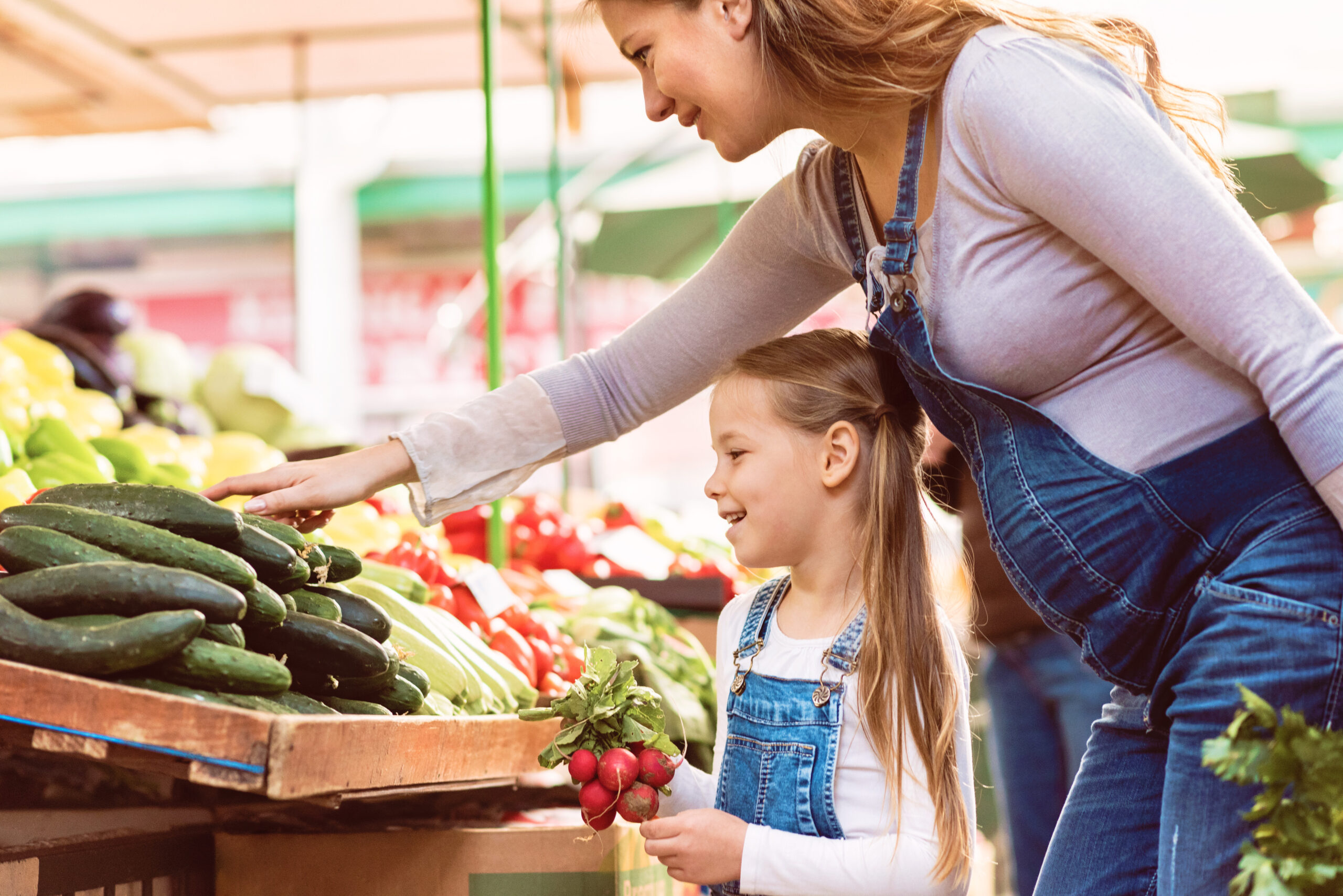 Pregnant mother and her daughter buying vegetables