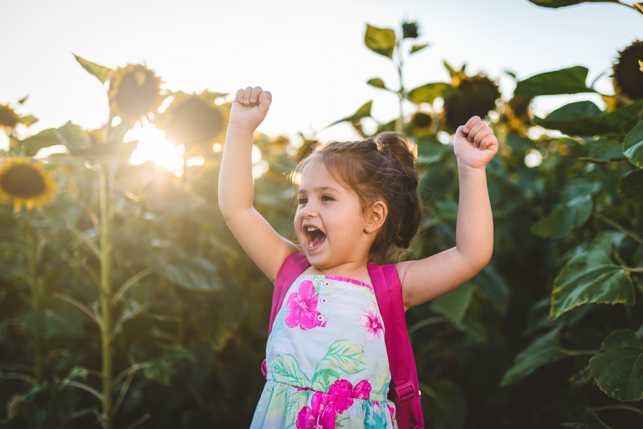 Cheerful and lovely child raising arms on a sunflower plantation