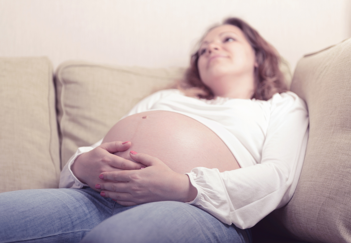 Pensive pregnant woman sitting on sofa at home