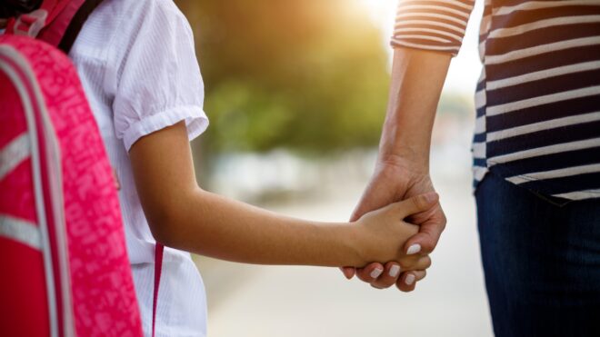 Mom and daughter holding hands outside of school