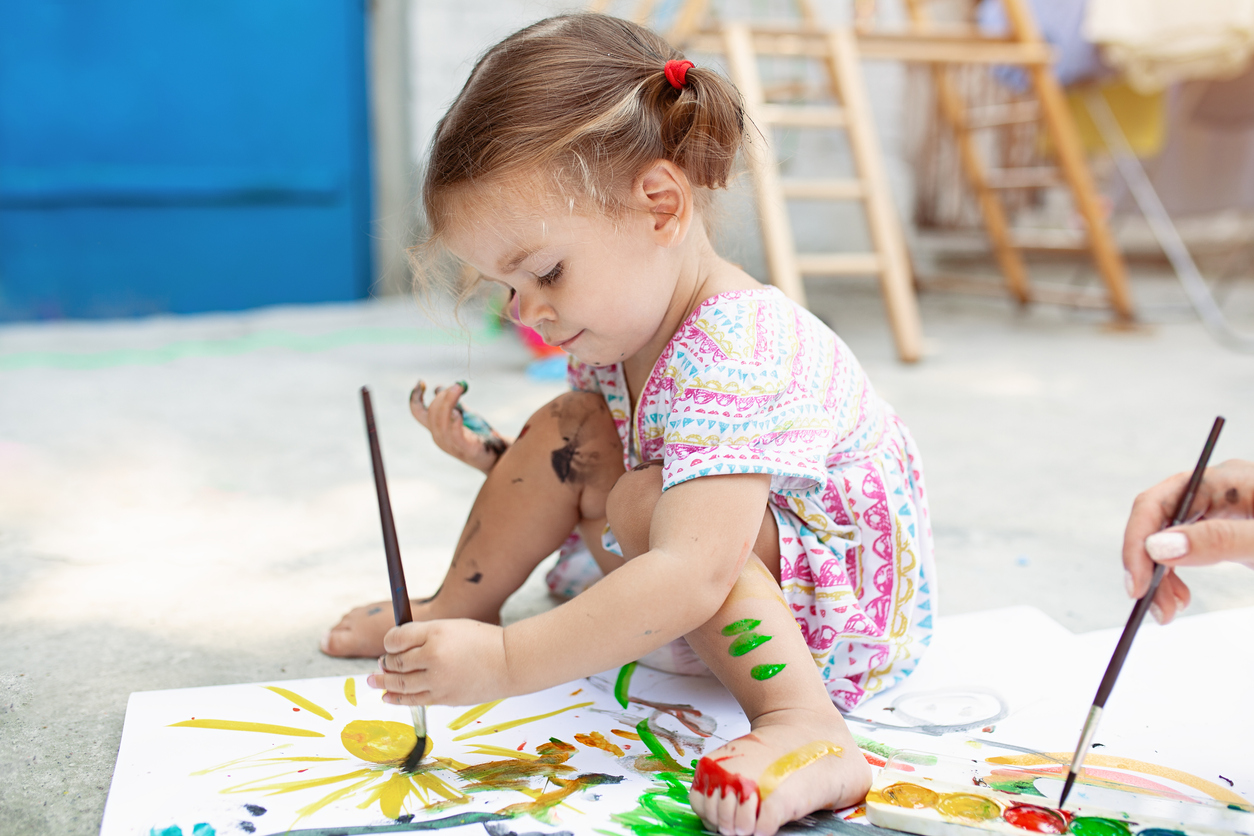 Cute little caucasian Girl enjoying Painting at the backyard with paper, water colour and art brush. Selective focus