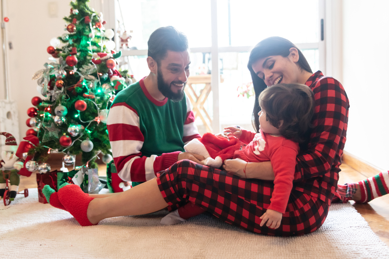 Beautiful family celebrating christmas wearing christmas pajamas and couple playing with their loving daughter at home