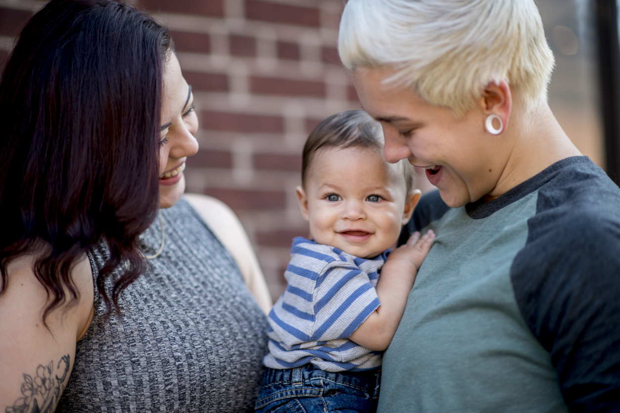 Young same sex couple adoringly smile at their baby boy