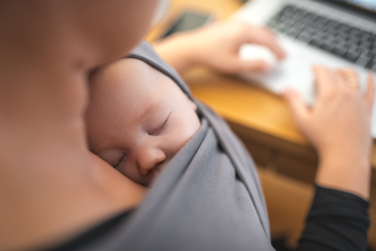 Young mother working from home with baby in baby carrier