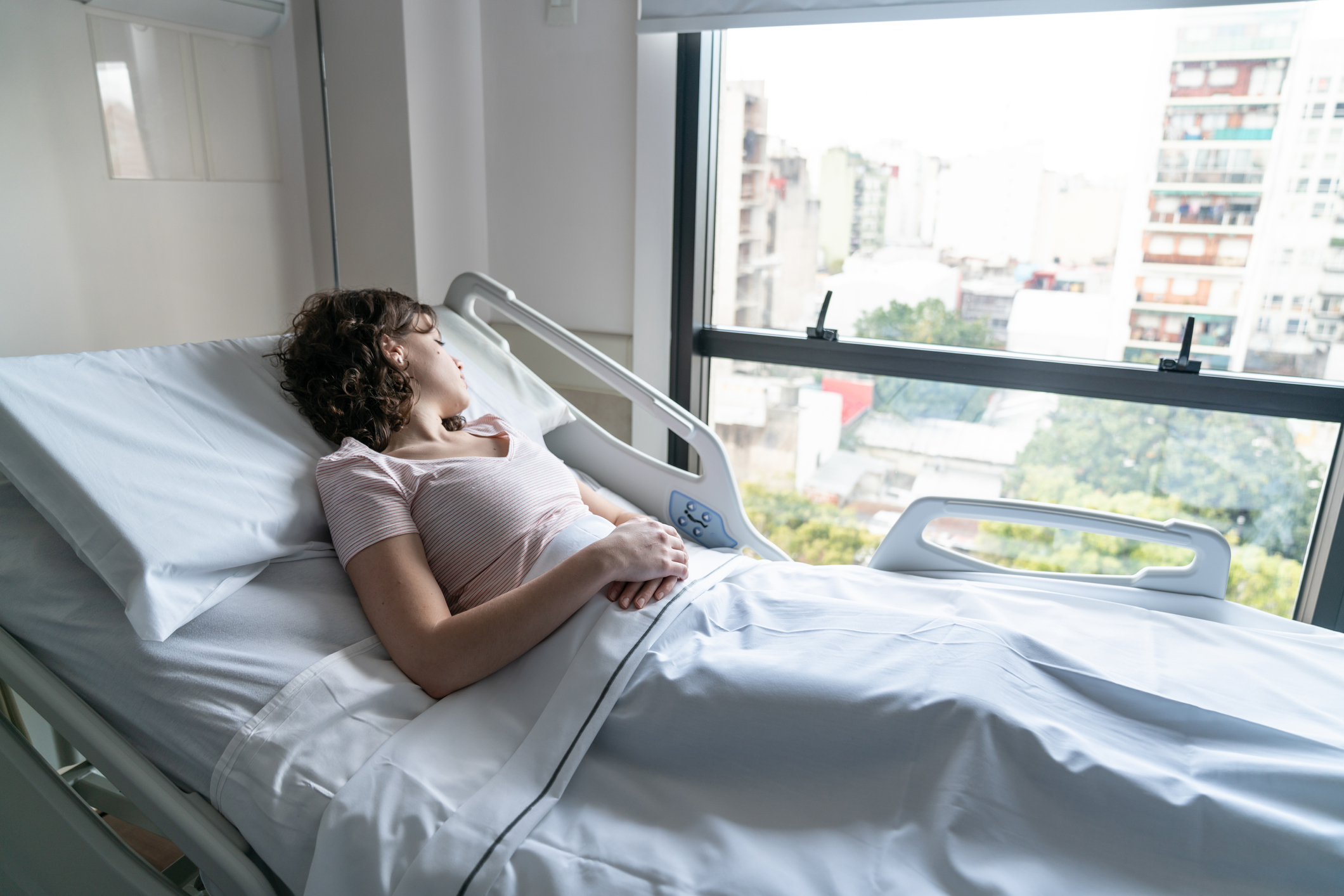 Young patient hospitalized lying down on bed looking to the window depressed