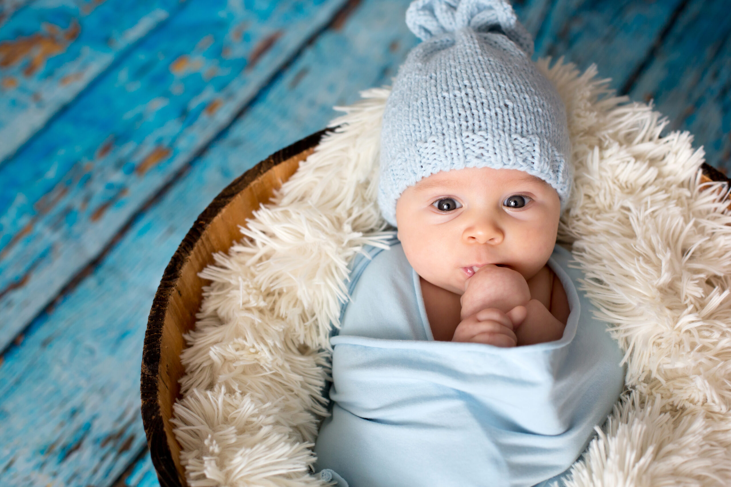 Little baby boy with knitted hat in a basket, happily smiling