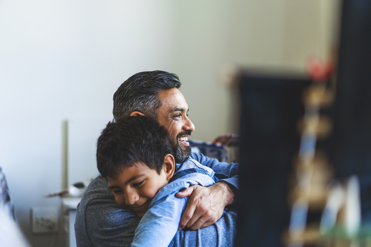 Smiling man embracing son in bedroom at home