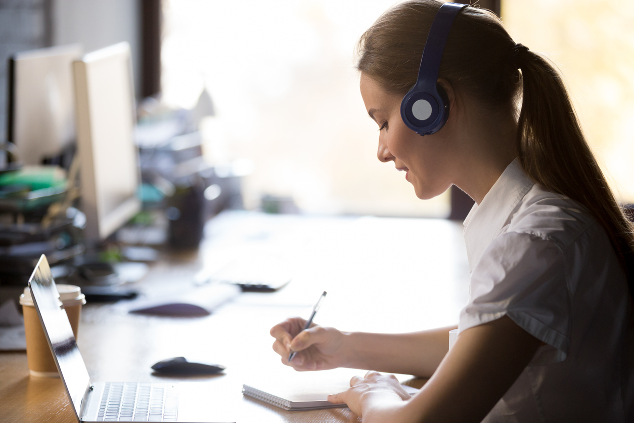 Focused woman wearing headphones write notes study online with teacher