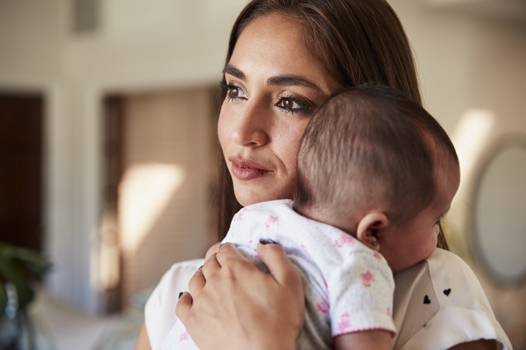 Millennial Hispanic mother holding her newborn son close to her chest, head and shoulders, close up