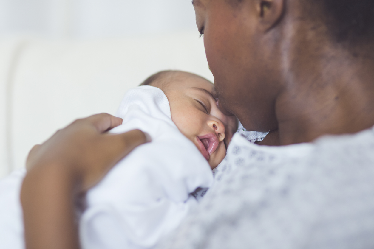 Beautiful African American mother in a hospital gown holds her newborn baby gently to her chest