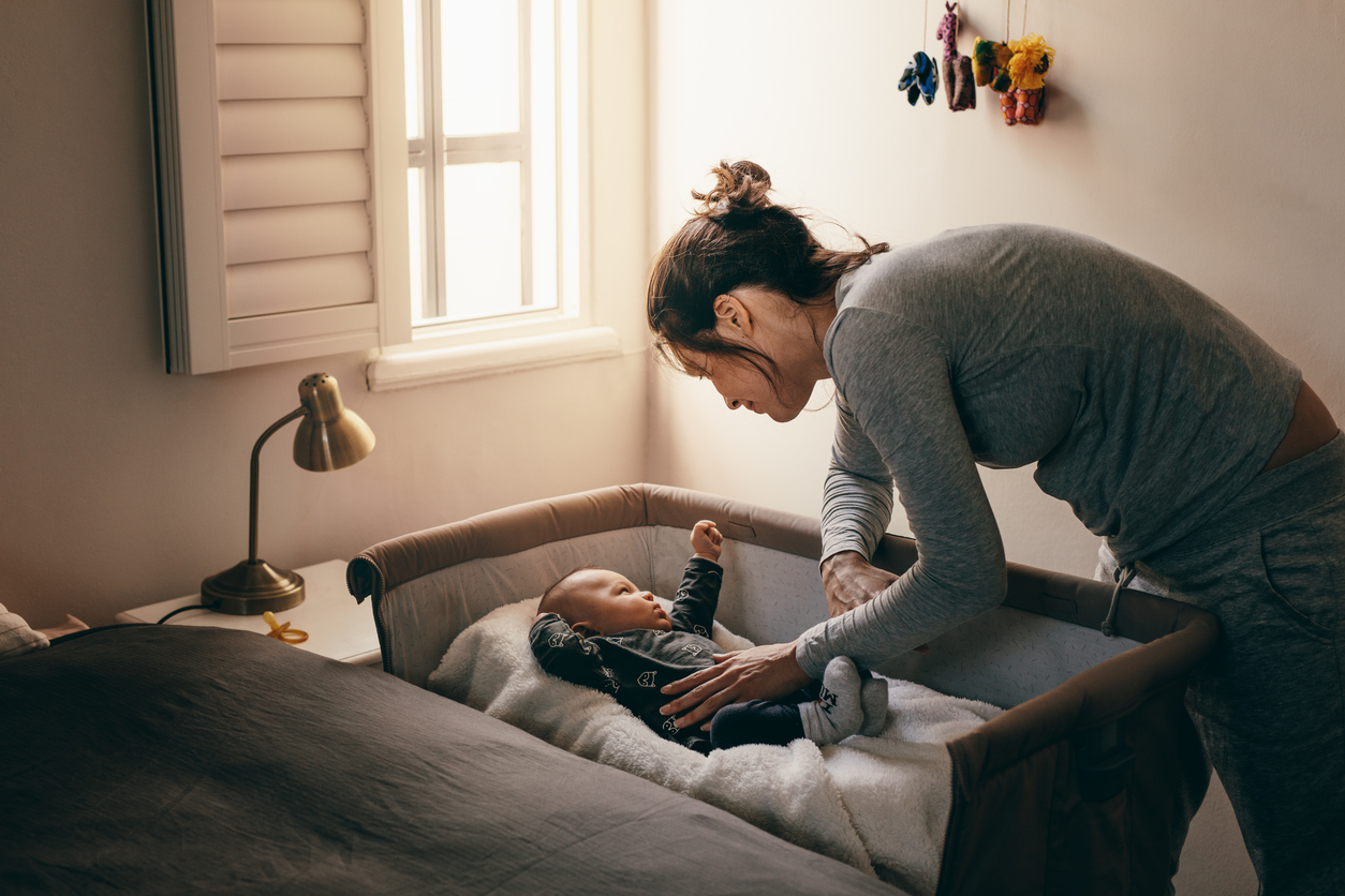 Young mother looking at her baby sleeping in a crib