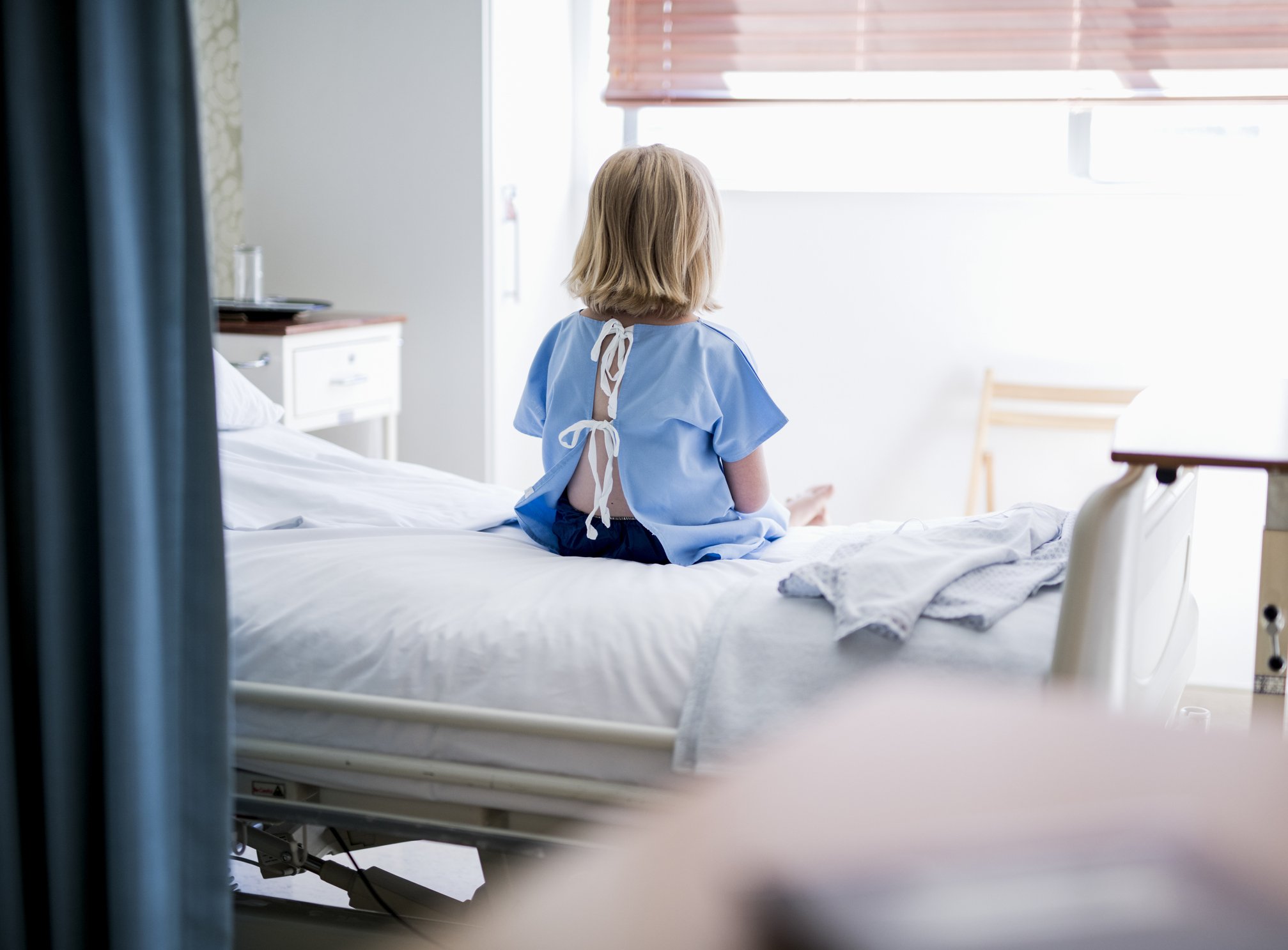 Rear view of sick girl sitting on bed at hospital