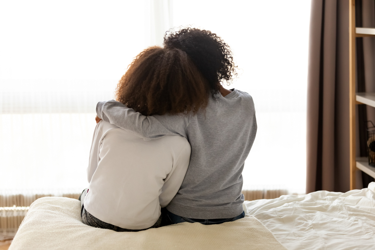 Rear view african mother and daughter embracing sitting on bed