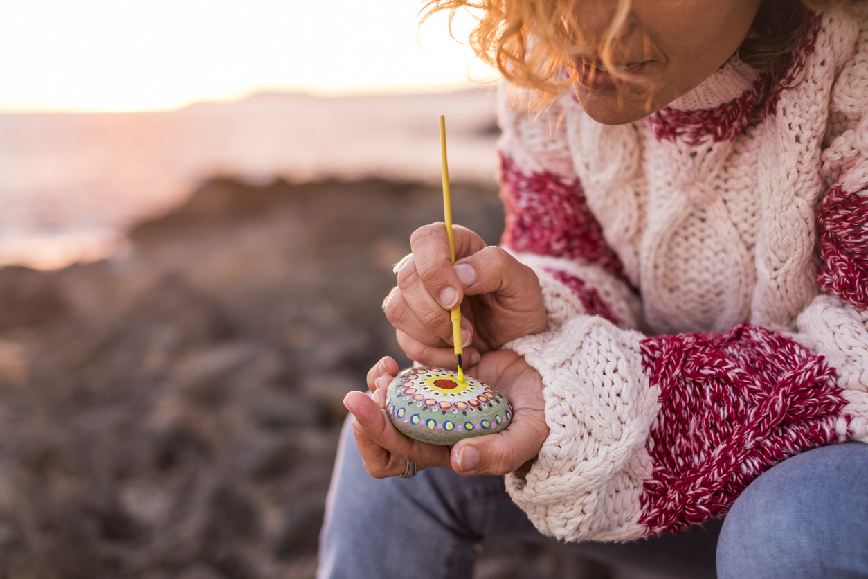 Hippy style concept female paint a mandala on a stone outdoor with sunset light in background - painting and diy hobby activity for artistic people - love and freedom concept