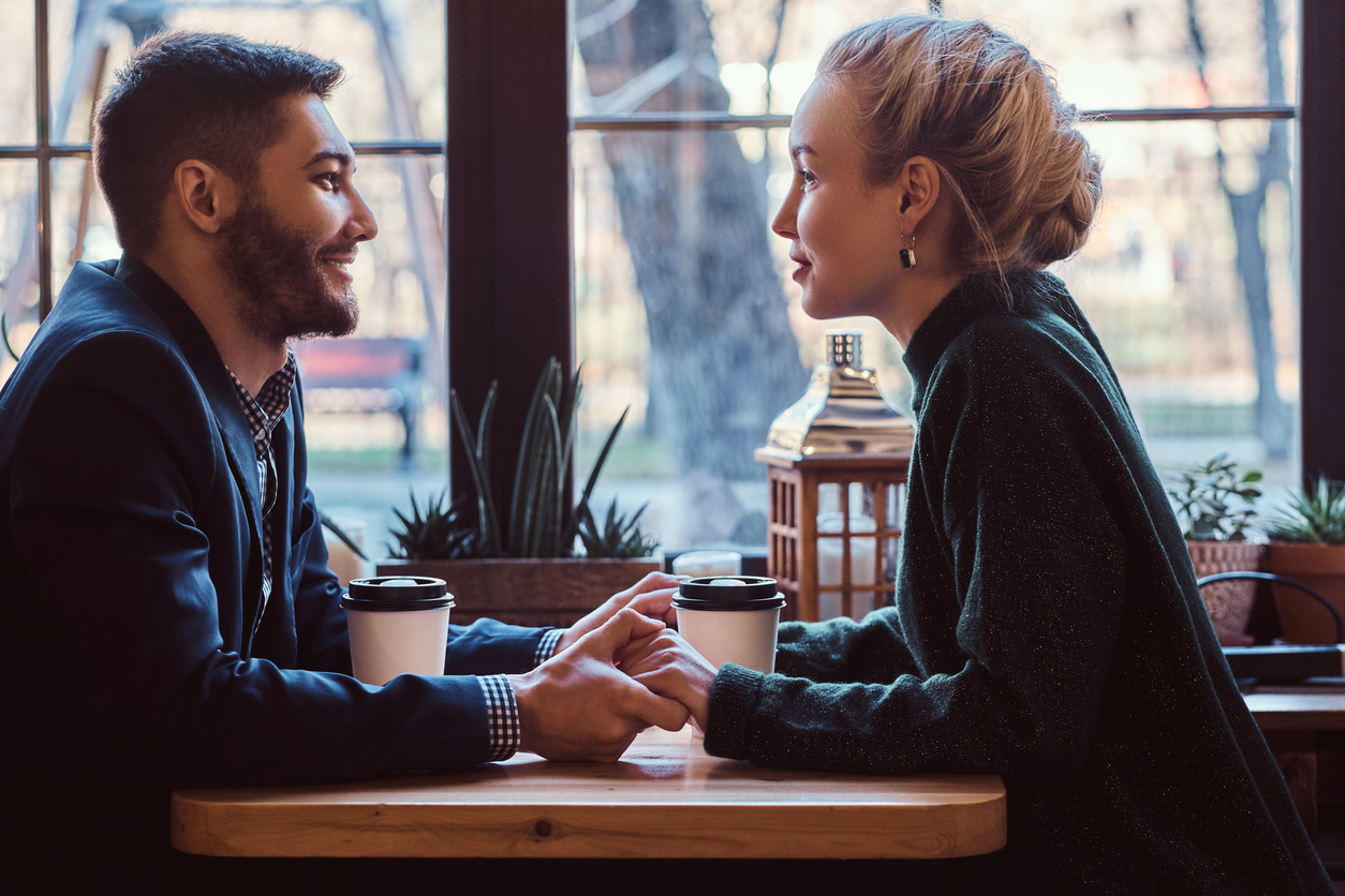 Attractive young couple holding hands, looking at each other and talking while sitting in the restaurant.