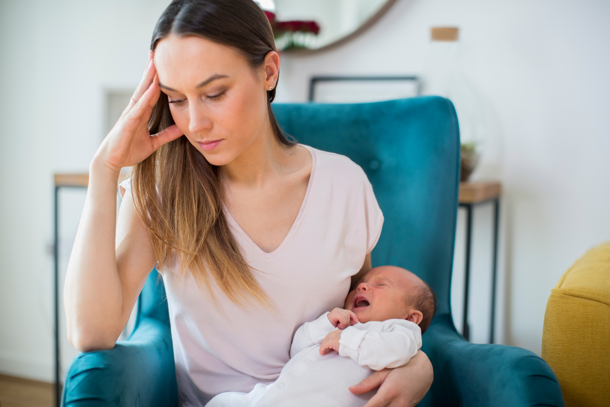 Stressed Mother Holding Crying Baby Suffering From Post Natal Depression At Home