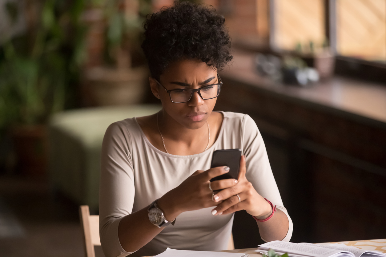 Upset confused african woman holding cellphone having problem with phone