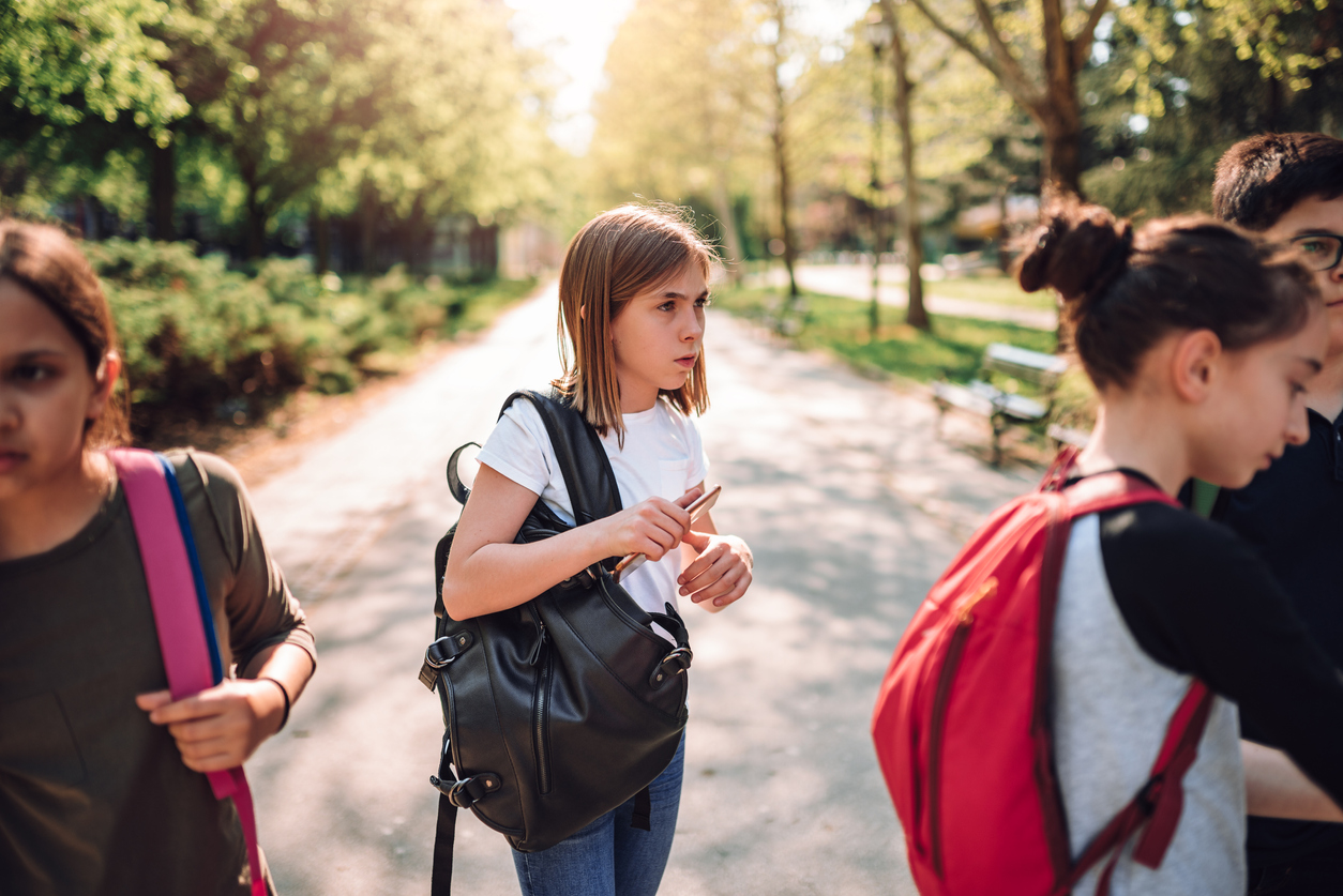 Confused schoolgirl standing in schoolyard with classmates