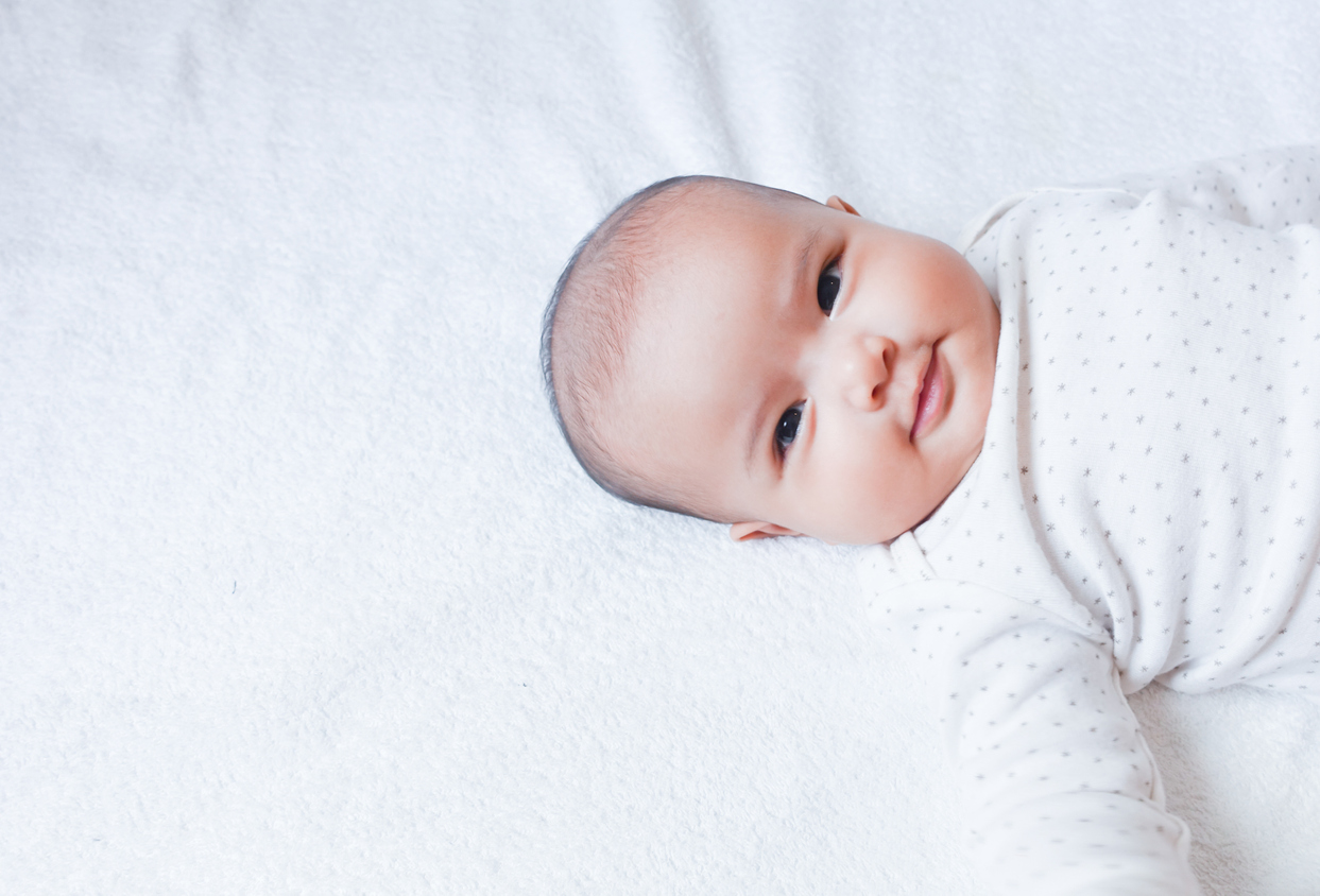 Asian baby girl lay down on the white bed sheet with little smile.