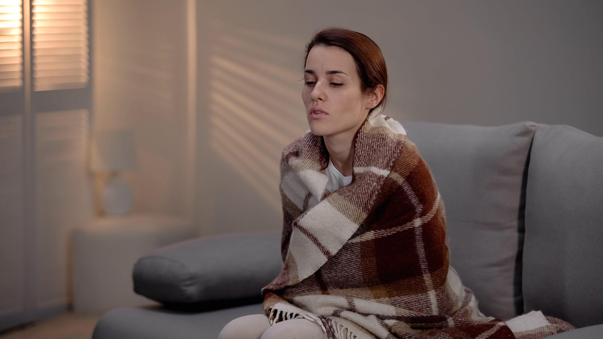 Terminally ill depressed young lady covered with plaid sitting alone in hospice