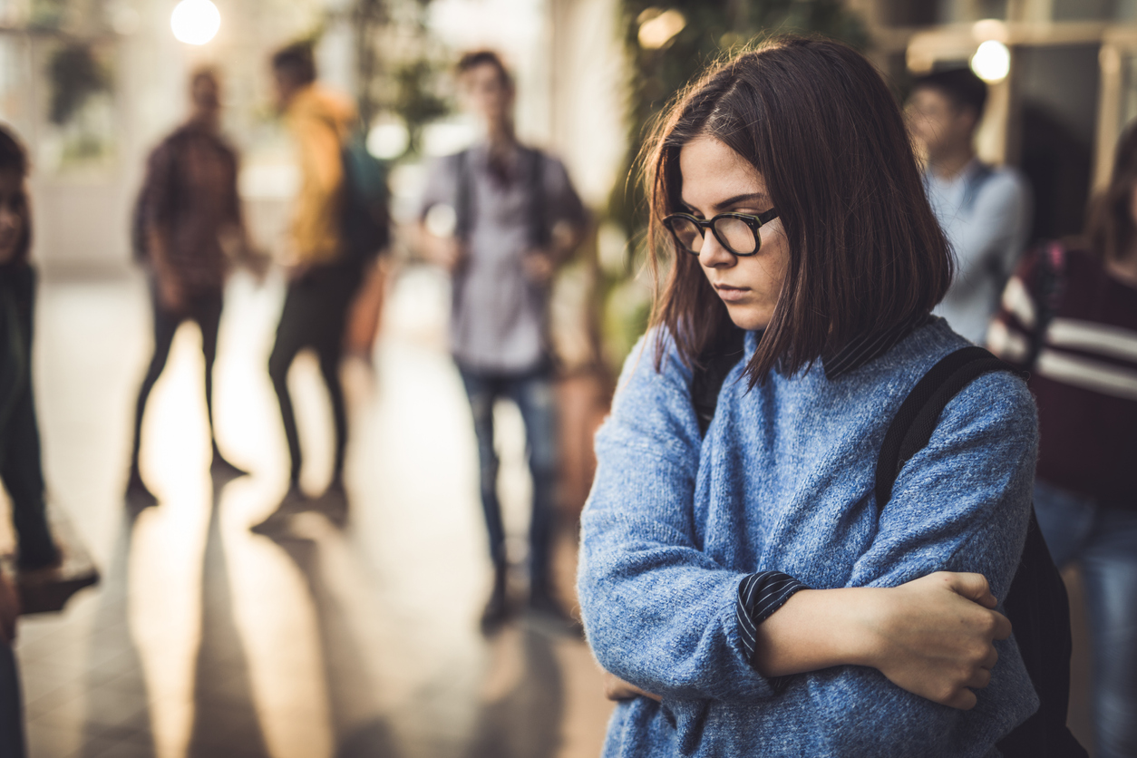 Sad high school student feeling lonely in a hallway.