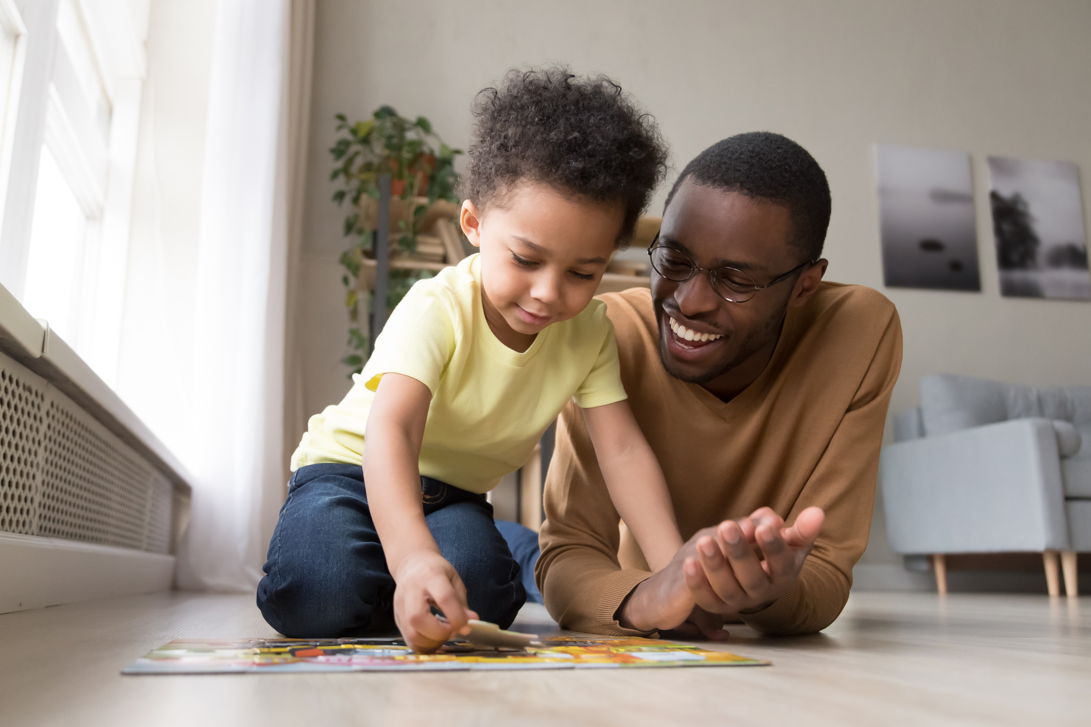 African father and little son collect jigsaw puzzle at home