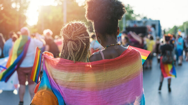 Young female couple hugging with rainbow scarf at the pride event