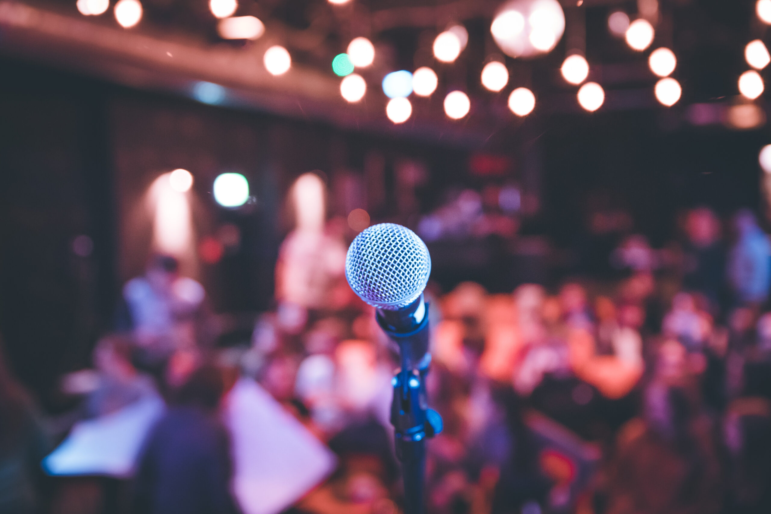 Event hall: Close up of microphone stand, seats with audience in the blurry background