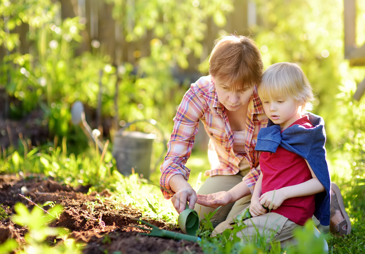 Little boy and woman planting seeds on beds in backyard.