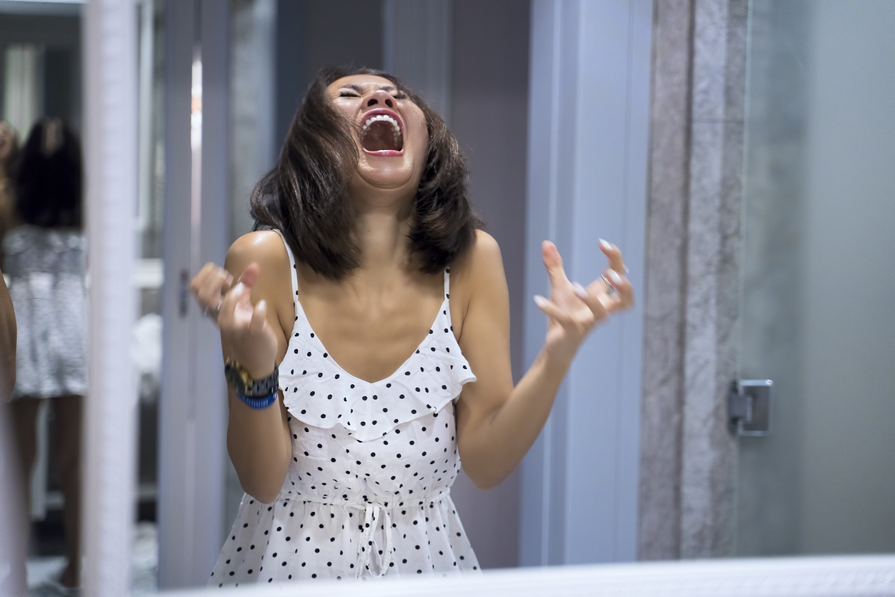 Angry woman shouting at mirror and crying