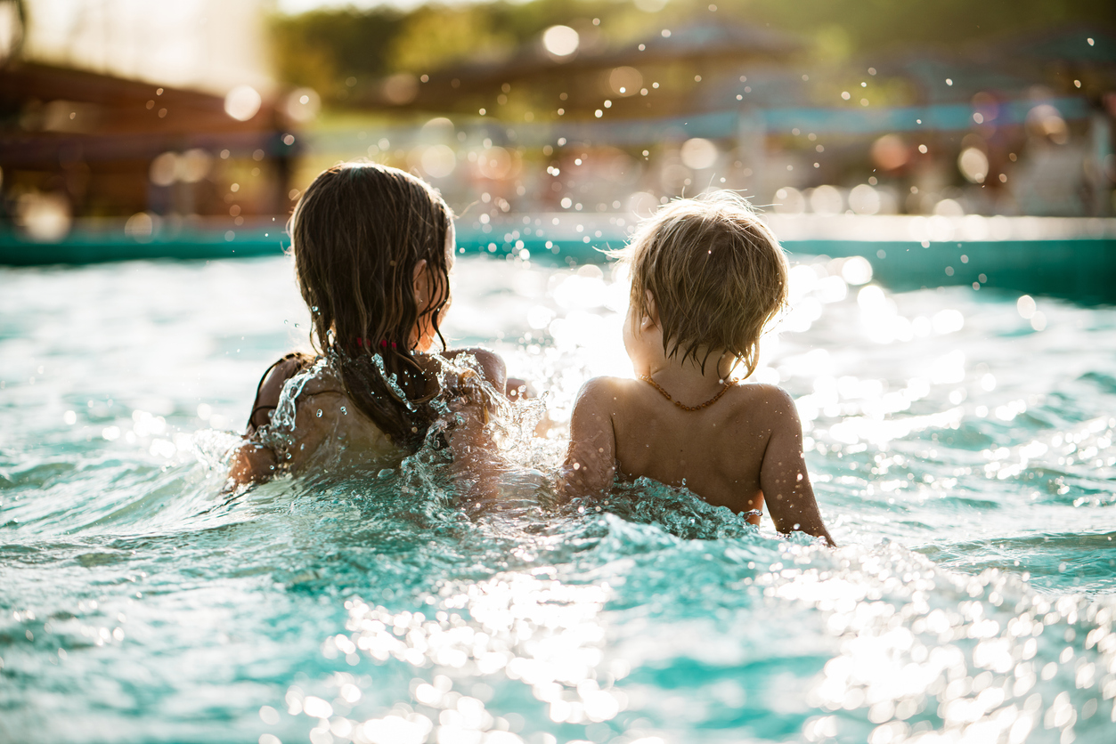 Rear view little boy and girl sitting and splashing in the pool