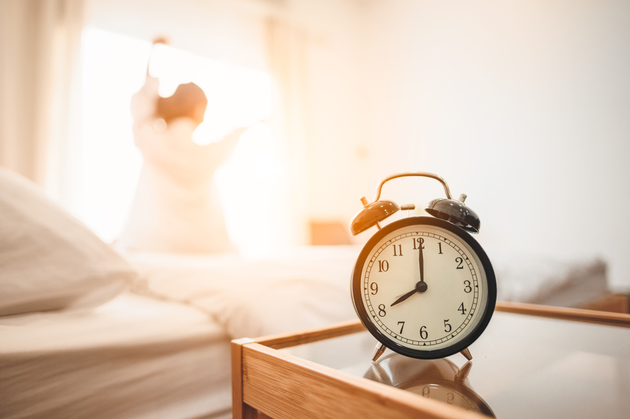 Closeup alarm clock  in bed after waking up, sunlight in morning.