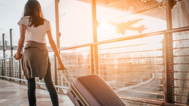 Young woman pulling suitcase in  airport terminal. Copy space